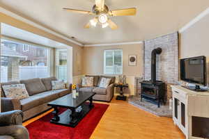 Living area with ceiling fan, ornamental molding, light wood-type flooring, and a wood stove