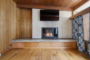 Detailed view of wood finished floors, a fireplace, a wooden ceiling with exposed beams, and wood walls