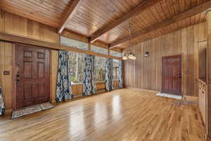 Foyer entrance featuring wooden walls, light wood-type flooring, a chandelier, wooden ceiling, and lofted ceiling with beams