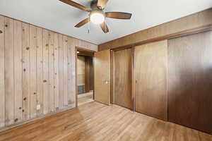 Unfurnished bedroom with light wood-style flooring, wooden walls, ceiling fan, and a closet