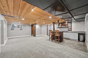 Below grade area with recessed lighting, wood ceiling, light colored carpet, and bar with sink