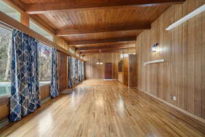 Empty room featuring wood walls, light wood-type flooring, and a wooden ceiling with exposed beams
