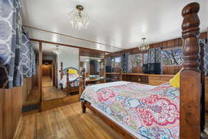 Bedroom with hanging lights, wood walls, and light wood-style flooring