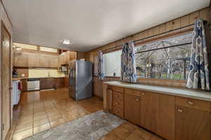 Kitchen featuring stainless steel appliances, light countertops, light tile patterned floors, wood finish cabinetry, and wood walls