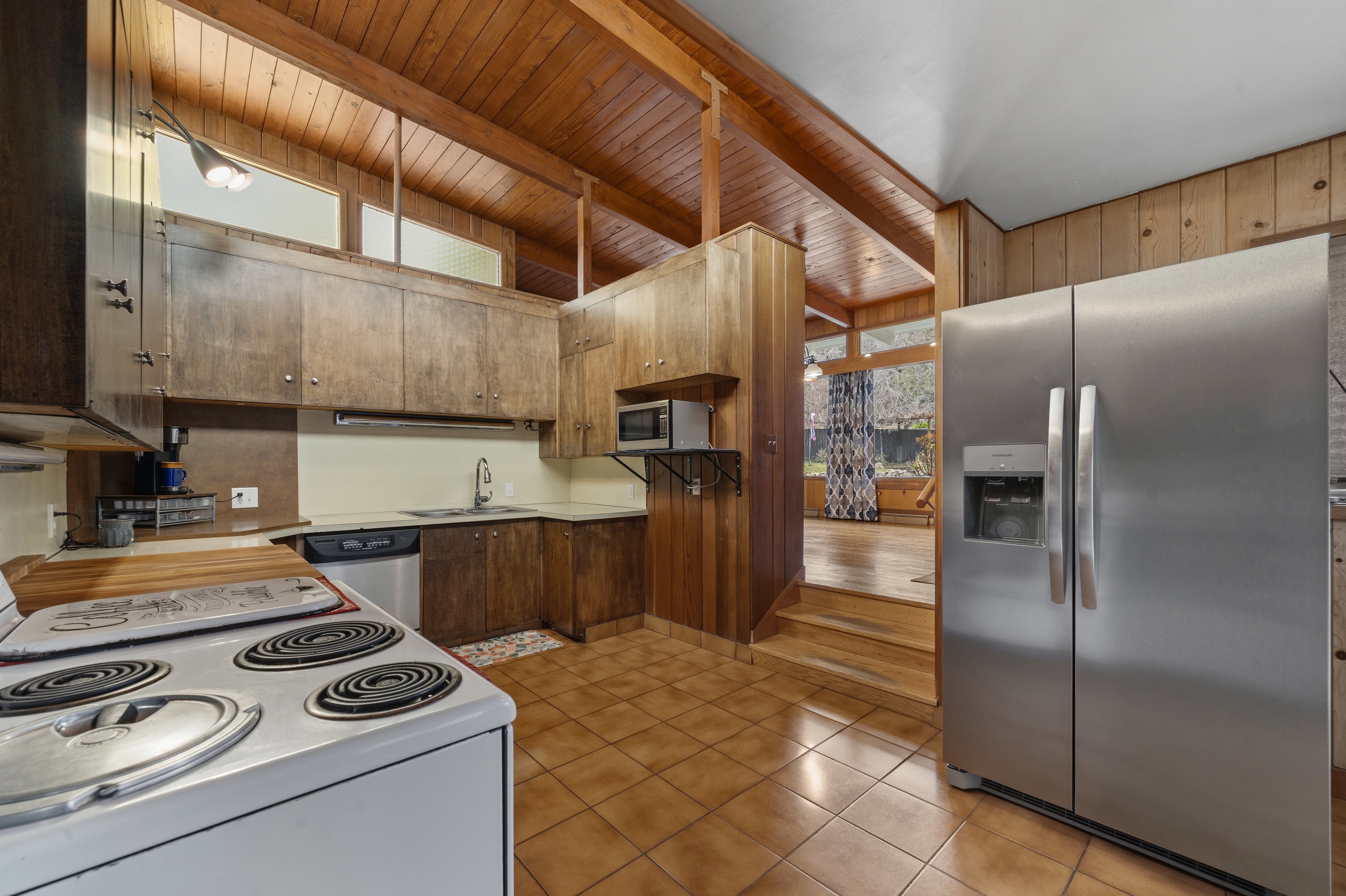 Kitchen featuring stainless steel appliances, light countertops, light tile patterned floors, a wooden ceiling with exposed beams, and wood walls