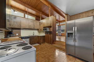 Kitchen featuring stainless steel appliances, light countertops, light tile patterned floors, a wooden ceiling with exposed beams, and wood walls