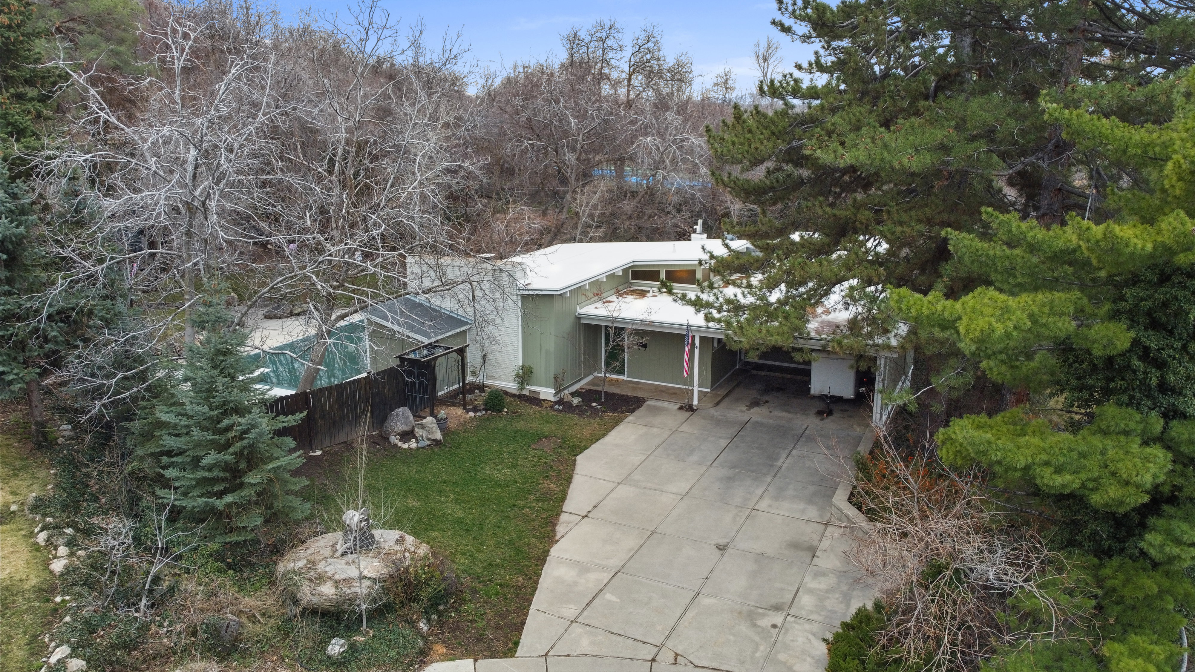 View of front of home featuring an attached carport, concrete driveway, and view of wooded area