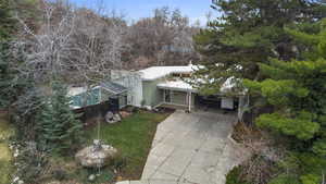 View of front of home featuring an attached carport, concrete driveway, and view of wooded area