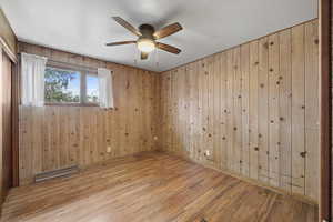 Spare room featuring hardwood / wood-style floors, ceiling fan, wood walls, and a baseboard radiator