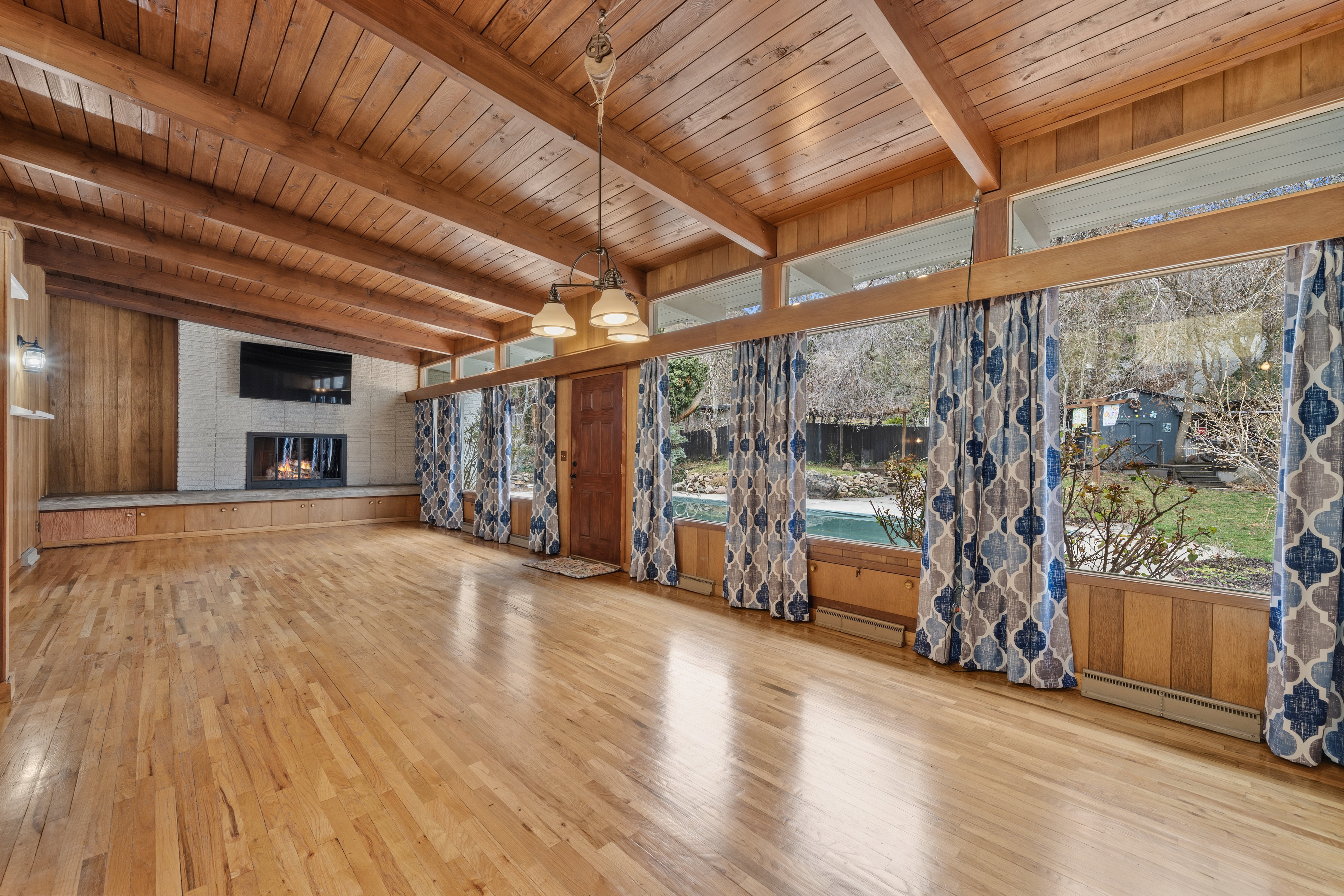 Unfurnished living room featuring light wood-type flooring, wood walls, a large fireplace, baseboard heating, and a wooden ceiling with exposed beams