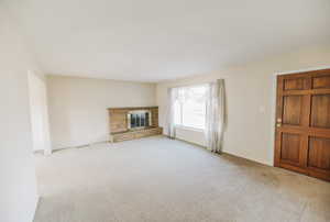 Unfurnished living room featuring light colored carpet and a stone fireplace