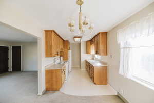 Kitchen featuring light countertops, white appliances, suspended lighting, light carpet, and wood finish cabinetry