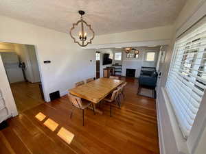 Dining room featuring suspended lighting, a fireplace, a textured ceiling, hardwood / wood-style floors, and stacked washer / dryer