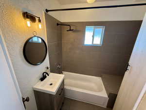 Full bathroom featuring a textured wall, vanity, and tub / shower combination