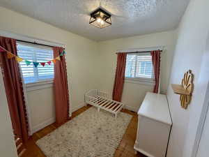 Bedroom with light wood finished floors, a nursery area, and a textured ceiling