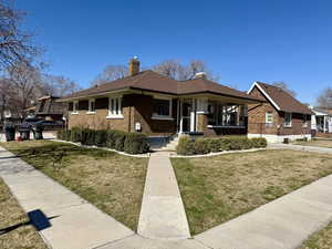View of front of home featuring a chimney, brick siding, a front yard, and covered porch