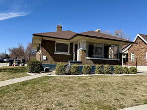 View of front of home featuring a porch, a chimney, a front lawn, and brick siding
