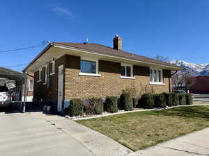 View of property exterior with brick siding, a chimney, a yard, and a mountain view