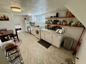 Kitchen featuring white appliances, a textured ceiling, open shelves, and white cabinetry