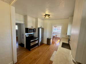 Kitchen with stainless steel appliances, a textured ceiling, light wood-type flooring, and light countertops