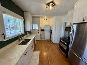 Kitchen with stainless steel appliances, light wood finished floors, a textured ceiling, stacked washer / drying machine, and white cabinets