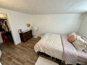 Bedroom featuring a textured ceiling, a spacious closet, and wood finished floors