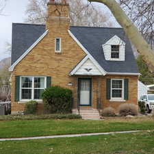 View of front of home with roof with shingles, a front yard, a chimney, and brick siding