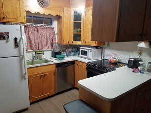 Kitchen featuring white appliances, wood finish cabinetry, light countertops, and a peninsula