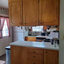 Kitchen with light countertops, freestanding refrigerator, wood finish cabinets, a peninsula, and plenty of natural light
