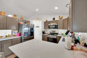 Kitchen with backsplash, stainless steel appliances, vaulted ceiling, a peninsula, and light stone counters