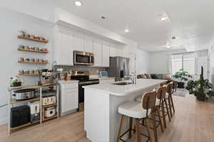 Kitchen featuring stainless steel appliances, white cabinets, a breakfast bar, an island with sink, and light wood finished floors