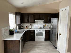 Kitchen featuring dark wood finish cabinets, vaulted ceiling, stainless steel appliances, light countertops, and decorative backsplash