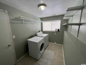 Laundry area featuring a textured ceiling, independent washer and dryer, and light tile patterned flooring