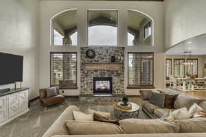 Carpeted living room with a high ceiling, a stone fireplace, plenty of natural light, and arched walkways