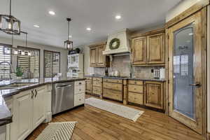Kitchen featuring dark stone counters, dishwasher, light wood-type flooring, tasteful backsplash, and hanging light fixtures