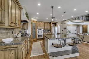 Kitchen with light wood-type flooring, hanging light fixtures, a kitchen bar, an island with sink, and stainless steel appliances