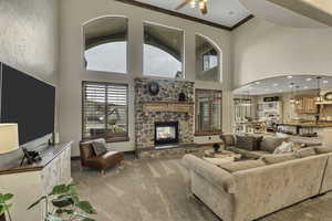 Living room featuring ornamental molding, light colored carpet, a stone fireplace, a ceiling fan, and arched walkways