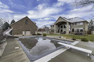 View of swimming pool featuring a diving board, a water slide, patio surround, a fenced backyard, and a hot tub