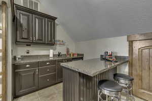 Kitchen with a kitchen breakfast bar, a peninsula, light stone countertops, light tile patterned floors, and dark wood finish cabinets