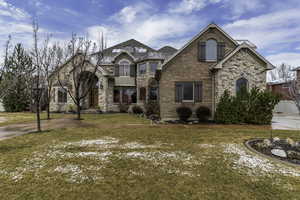 View of front of property featuring brick siding, a front yard, a balcony, and stone siding