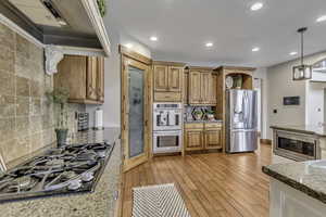 Kitchen with stainless steel appliances, light stone counters, decorative light fixtures, wood finish cabinetry, and light wood finished floors