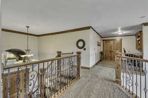 Corridor featuring a chandelier, ornamental molding, an upstairs landing, and light carpet