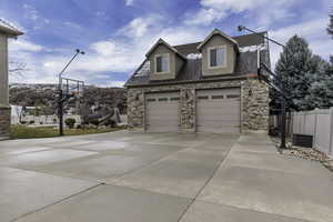 View of front facade featuring a shingled roof, stone siding, and driveway