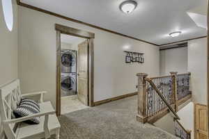 Corridor featuring an upstairs landing, light colored carpet, ornamental molding, stacked washer / dryer, and light tile patterned flooring