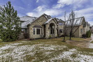 View of front facade featuring a lawn, stone siding, and a high end roof