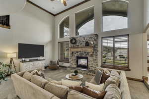 Carpeted living area featuring a high ceiling, a stone fireplace, ornamental molding, healthy amount of natural light, and ceiling fan