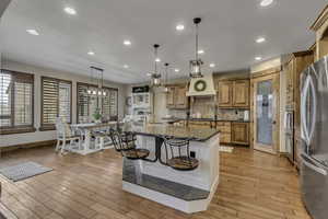 Kitchen featuring an island with sink, stainless steel appliances, dark stone countertops, and hanging light fixtures