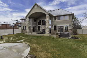 Back of property with stucco siding, a patio area, a hot tub, and a shingled roof