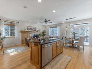 Kitchen with a kitchen island with sink, light wood finished floors, stainless steel dishwasher, a fireplace, and wood finish cabinets