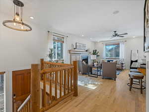 Living area with light wood-style flooring, healthy amount of natural light, a ceiling fan, a warm lit fireplace, and recessed lighting